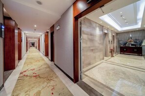 A hotel corridor with a carpeted floor, wooden walls, and a glass door leading to a room with a bed and a desk. - Harmonious Qianjin Hotel (Kaili)