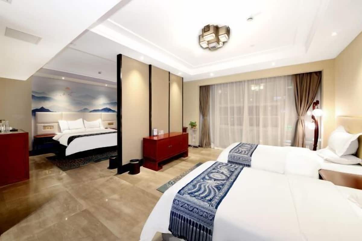 A hotel room with a large bed, a red dresser, a nightstand, and a wall-mounted light fixture.