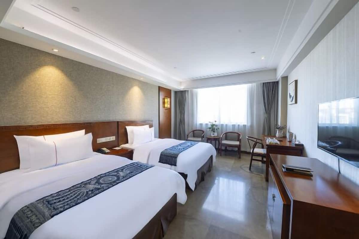 A hotel room with two beds, a desk, a chair, a TV, and a window with curtains.