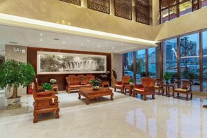 A spacious lobby with a high ceiling, large windows, and traditional wooden furniture. - Harmonious Qianjin Hotel (Kaili)