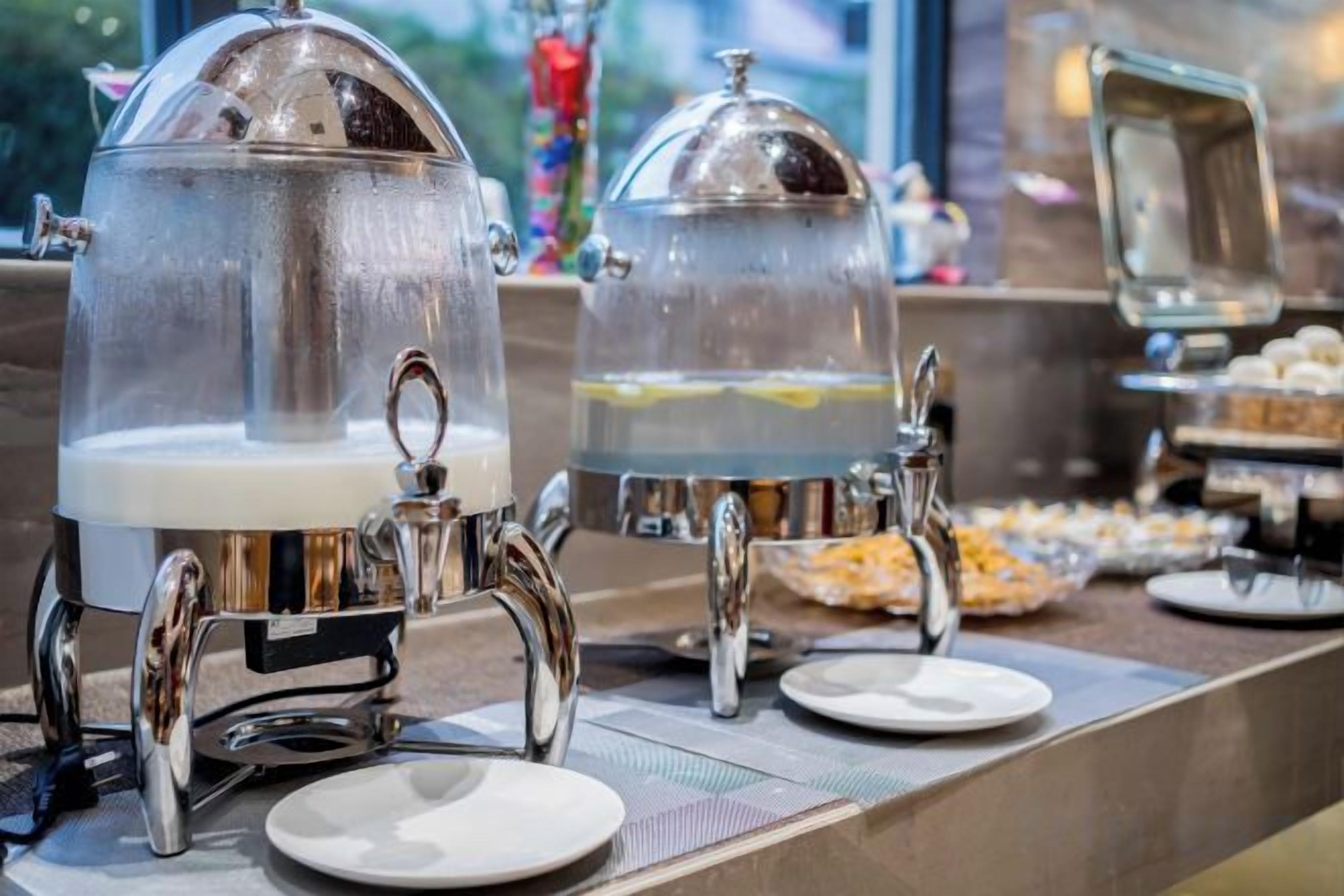 A buffet setup with two clear glass dispensers, likely for beverages, and a variety of food items on the counter.