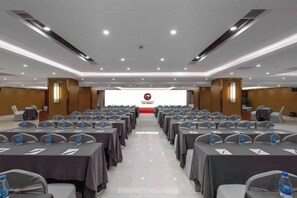 A conference room with rows of tables and chairs, a podium at the front, and a logo on the wall. - Harmonious Qianjin Hotel (Kaili)