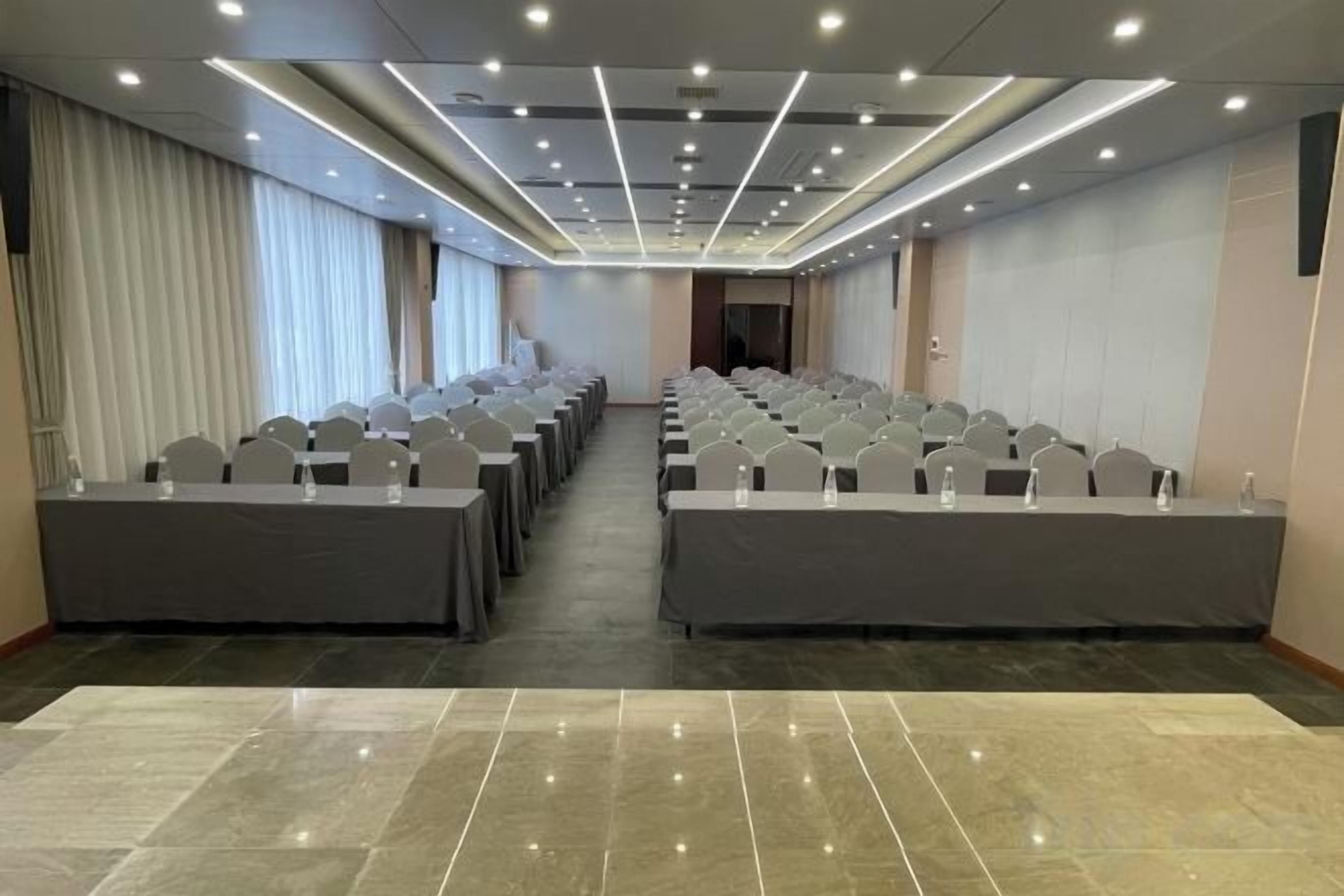 A conference room with rows of tables and chairs, a long table at the front, and a carpeted floor.
