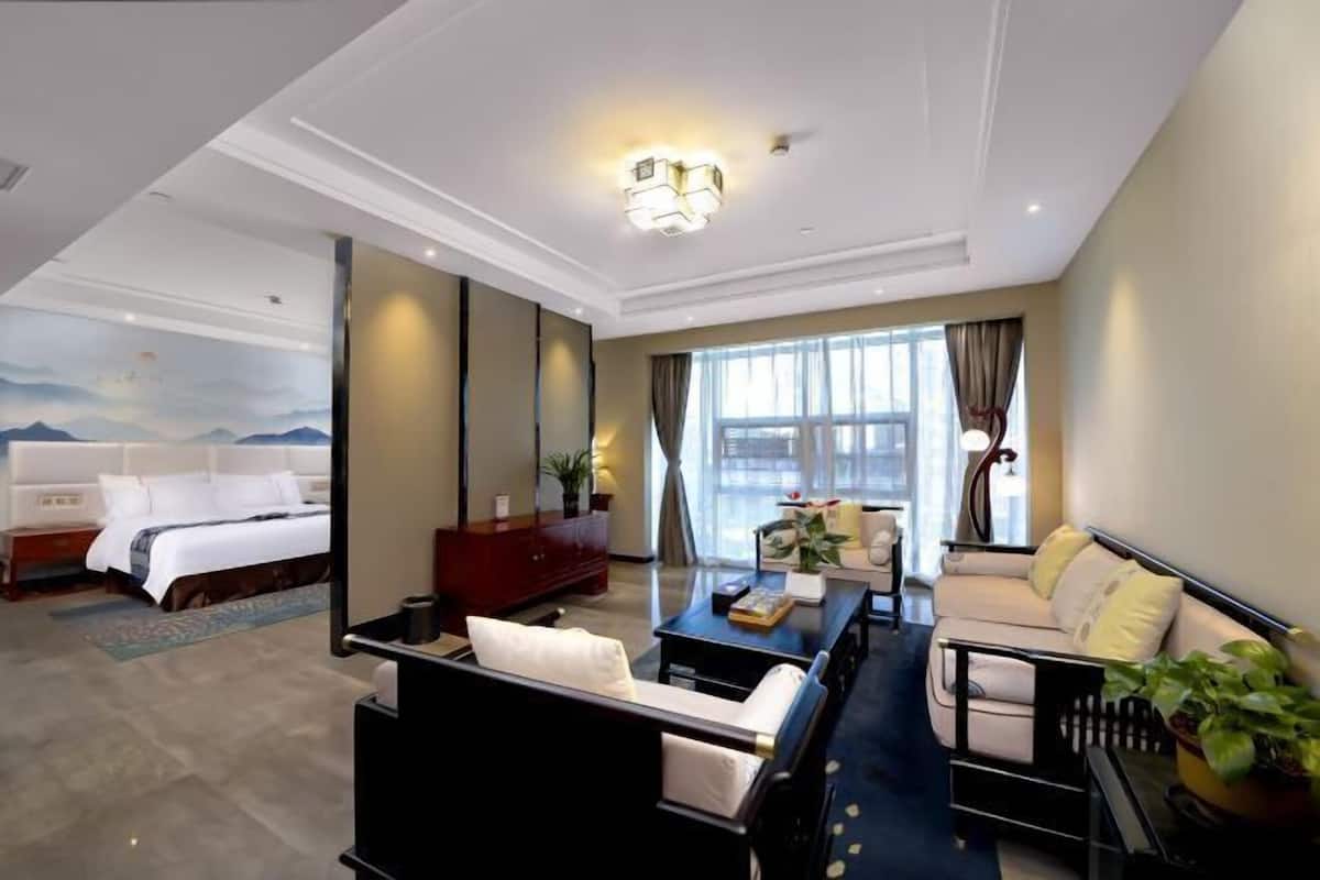 A hotel room with a bed, a sofa, a coffee table, a desk, and a large window.