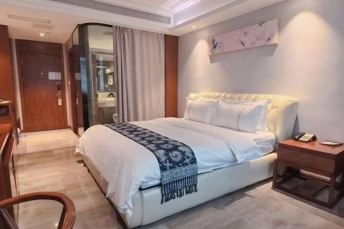 A hotel room with a large bed, a bedside table with a phone, a mirror, and a door leading to a bathroom.