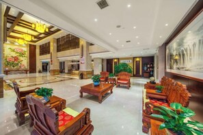 A spacious lobby with a high ceiling, a central seating area with wooden furniture, and a large painting on the wall. - Harmonious Qianjin Hotel (Kaili)