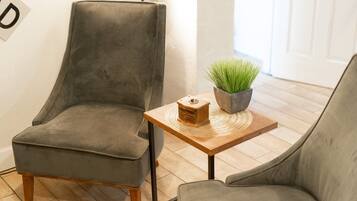 Una habitación con un sillón tapizado gris, una mesita de madera con un mantel tejido y una planta en maceta.