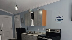 A kitchen with grey cabinets, a black refrigerator, a stove, and a dining table with chairs. - Redfish 'n Relaxation (Aransas Pass)