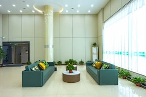 Um hall amplo com teto alto, uma mesa redonda central e áreas de estar.
