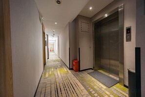 Un couloir d’hôtel avec un sol à motifs, un ascenseur et une poubelle.