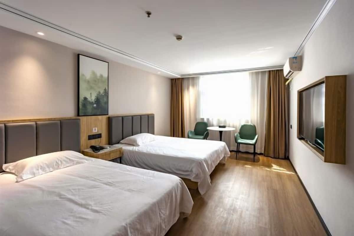 Une chambre d’hôtel avec deux lits, un bureau, une chaise, une petite table, une fenêtre avec des rideaux et un téléviseur fixé au mur.
