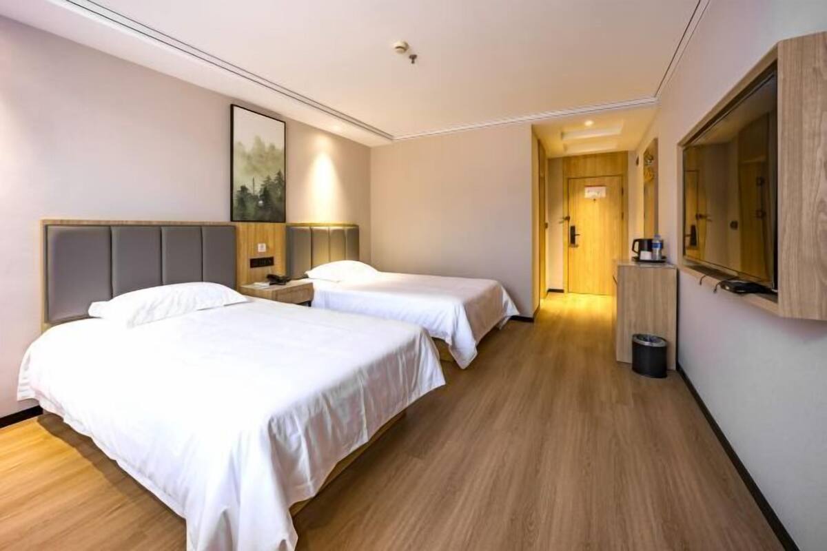 Une chambre d’hôtel avec deux lits, un plancher en bois, un grand miroir et un tableau encadré au mur.