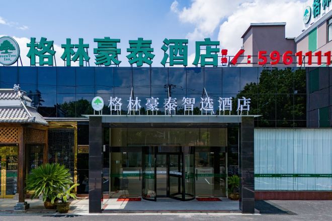 A hotel entrance with a traditional architectural style, a modern glass facade, and a contact number displayed above the entrance.