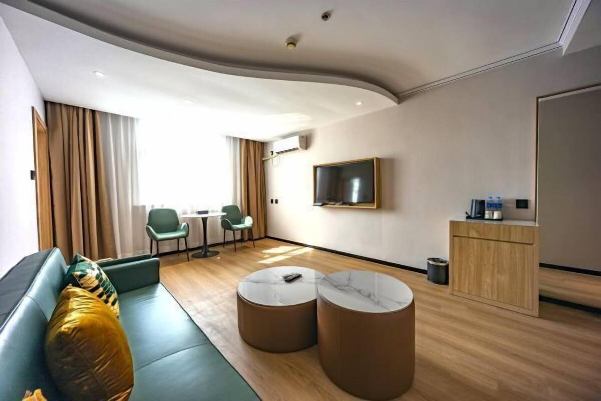 Une chambre d’hôtel moderne équipée d’un canapé, de deux petites tables rondes, d’un téléviseur fixé au mur et d’un petit coin cuisine.