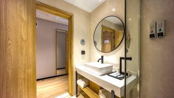 A modern bathroom with a wooden floor, a white sink with a mirror, and a glass shower enclosure.