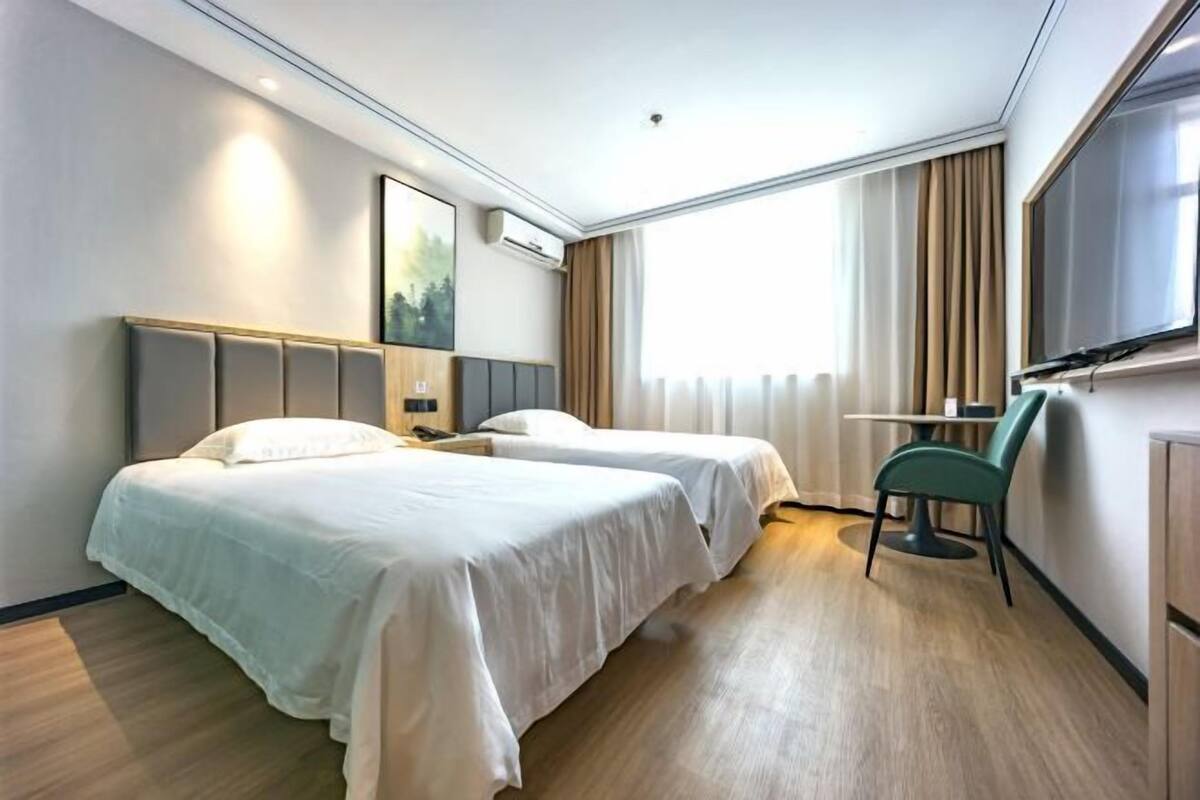 Une chambre d’hôtel avec deux lits, un bureau, une chaise, une télévision et une grande fenêtre avec des rideaux.
