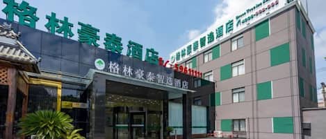 A hotel with a traditional Chinese architectural entrance, a modern building with green accents, and a parking lot.