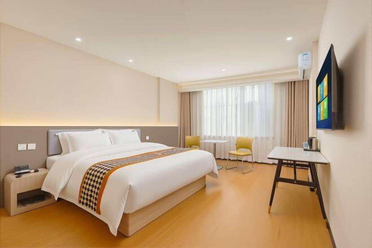 A hotel room with a bed, bedside table, chair, desk, and a TV mounted on the wall.