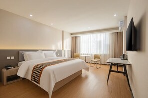 A hotel room with a bed, bedside table, lamp, chair, and a TV on the wall. - Jincheng Hotel (Yinan)