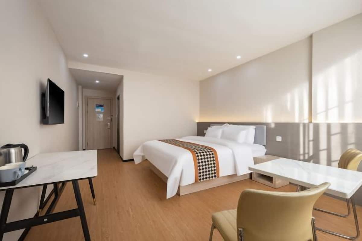 A hotel room with a bed, a desk, a chair, a television, and a bathroom door.