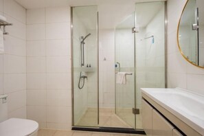 Un baño moderno con ducha envuelta en vidrio, inodoro blanco y un espejo grande.