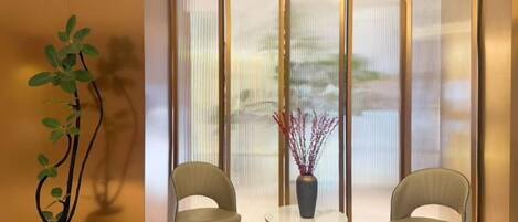 A room with two chairs, a small table, a potted plant, and a view through a partition.