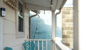 A covered porch with turquoise metal chairs and a small table, a brick wall, and a view of the ocean. - Cozy Rehoboth Beach 2BR Retreat - Just 1.5 Blocks to the Beach! (Rehoboth Beach)
