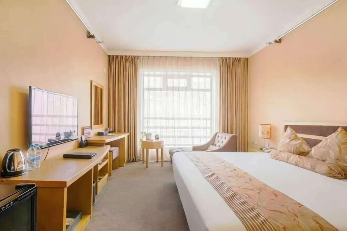 A hotel room with a bed, desk, chair, TV, and a window with curtains.