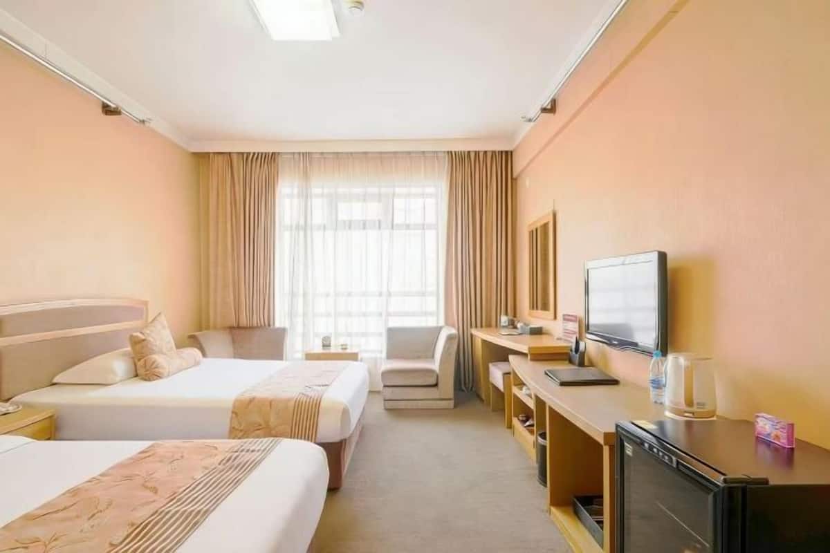 A hotel room with two beds, a desk, a television, and a minibar.