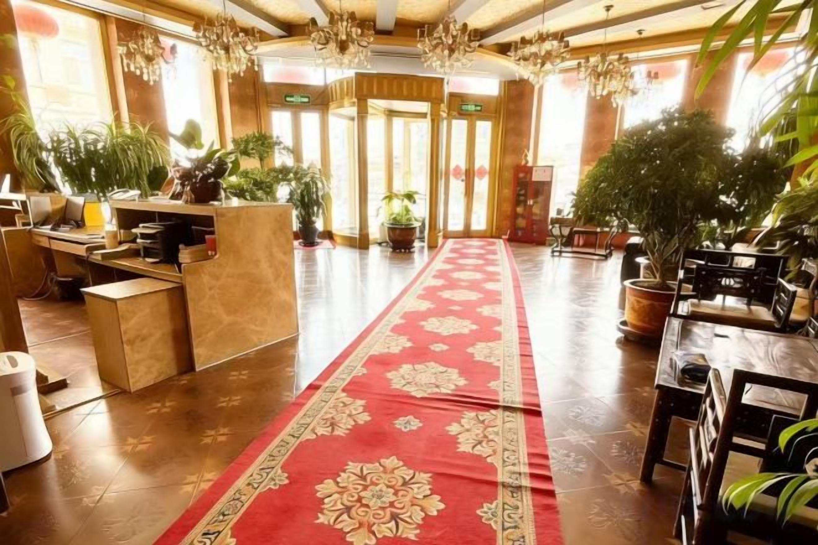 Un vestíbulo de hotel con mostrador de recepción, alfombra roja y plantas en macetas.