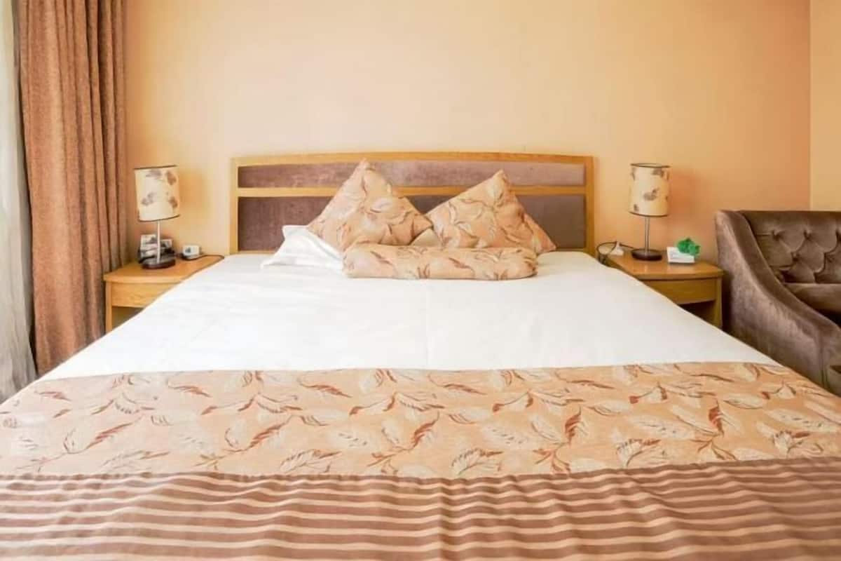 A hotel room with a bed, two nightstands, a lamp, a chair, and a curtain.