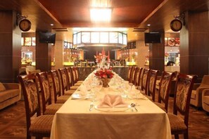 Una larga mesa de comedor dispuesta para una comida formal, flanqueada por sillas de madera con asientos acolchados.