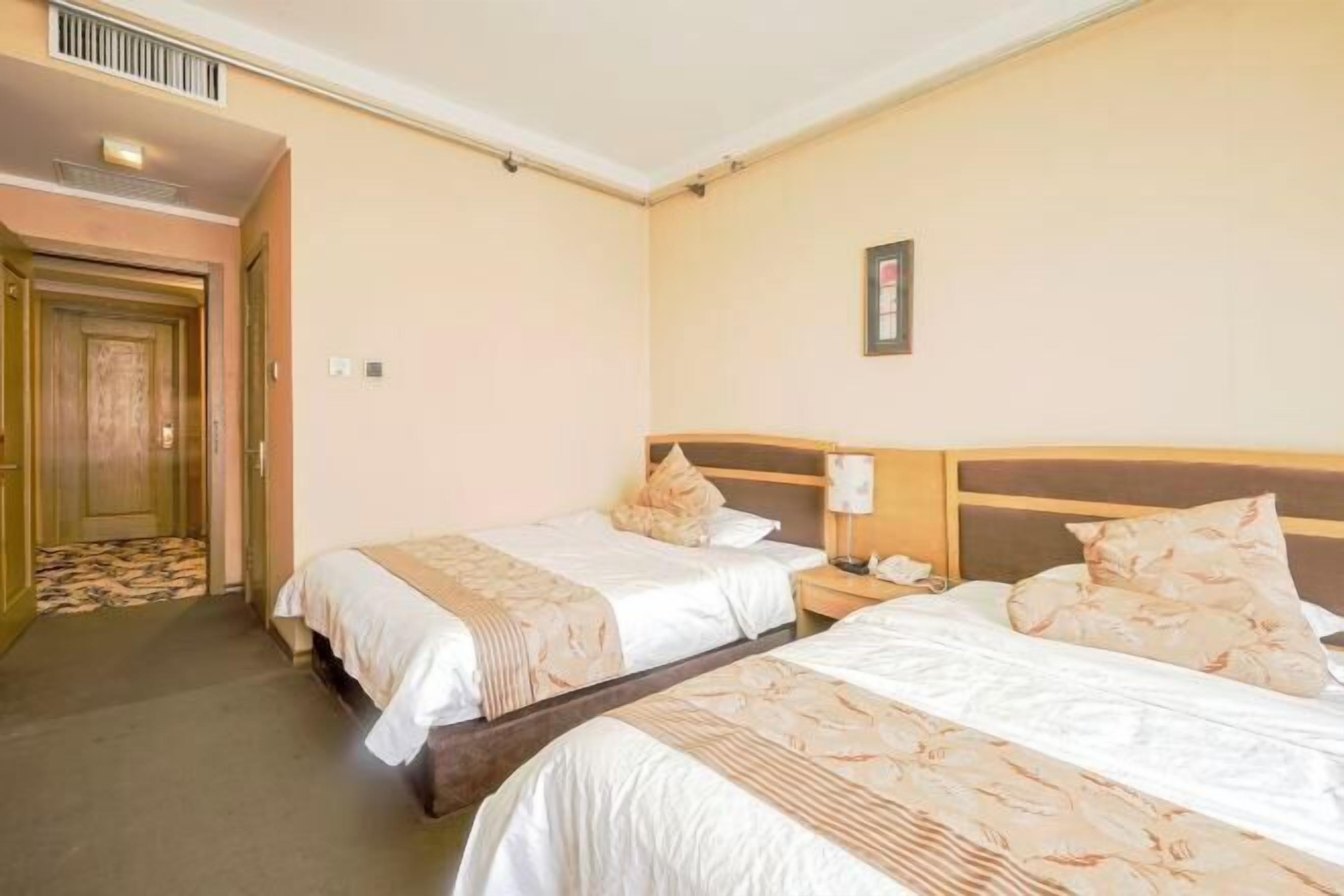 Una habitación de hotel con dos camas, un cabecero de madera, una mesita de noche y una puerta que da a un pasillo.