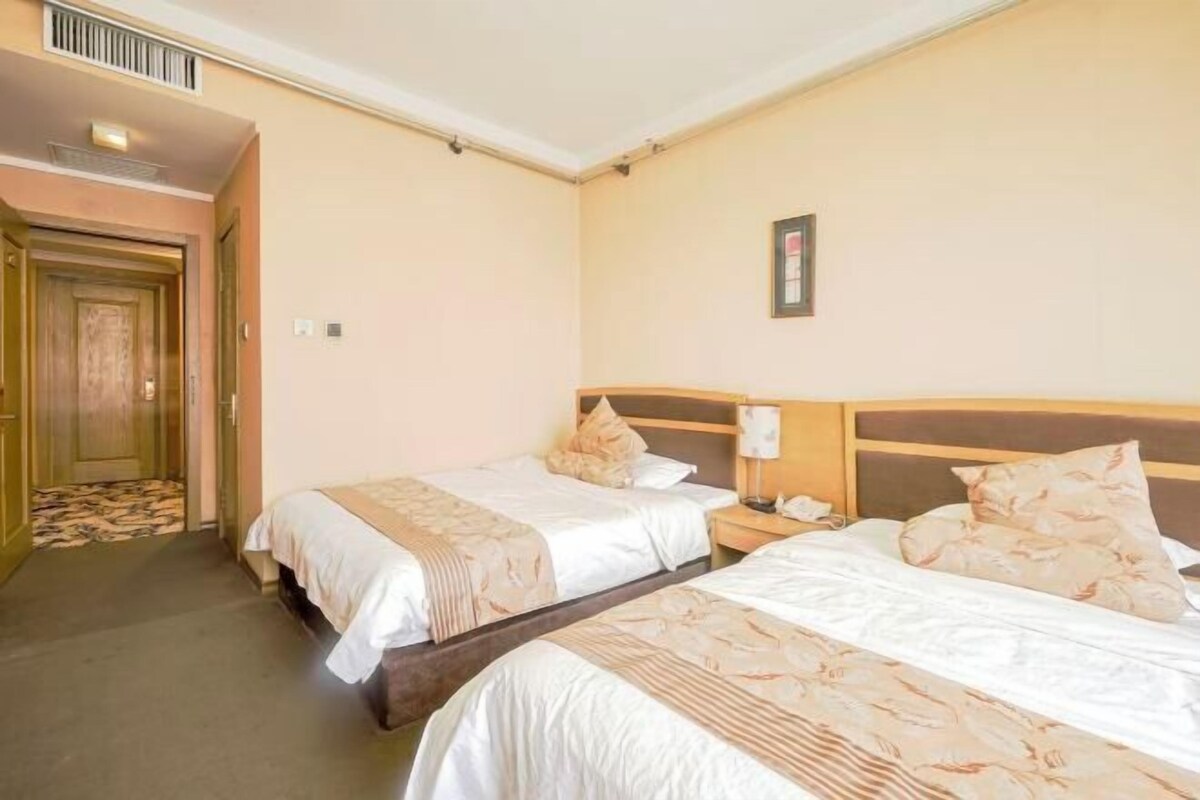 A hotel room with two beds, a wooden headboard, a nightstand, and a door leading to a hallway.