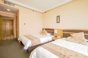 A hotel room with two beds, a wooden headboard, a nightstand, and a door leading to a hallway.
