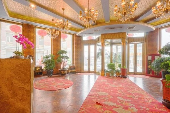 A hotel lobby with a grand chandelier, a red carpet, and potted plants. - Ping'an Business Hotel (Harbin)