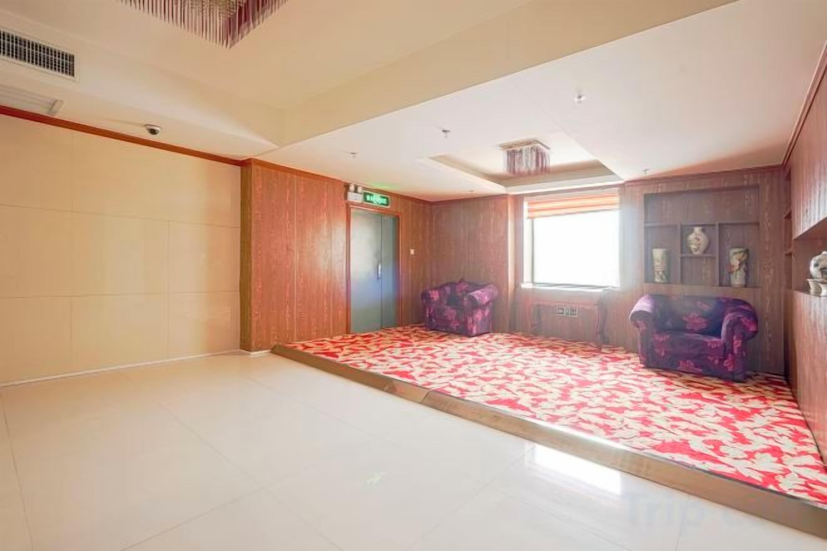 Habitación de hotel con una cama grande, un armario de madera, una ventana con persianas y un tapete estampado rojo.