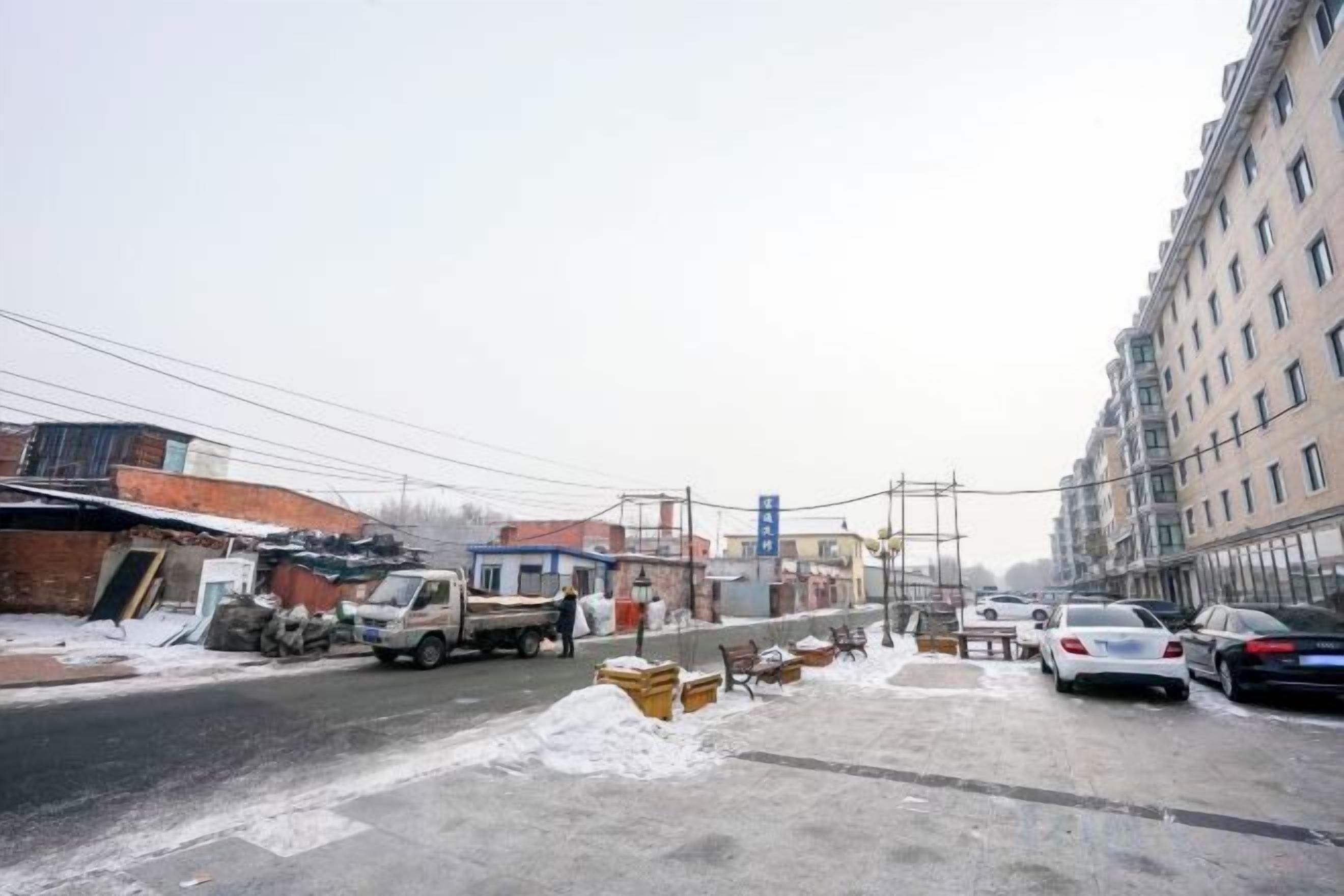 A street scene with buildings, parked cars, and a truck.