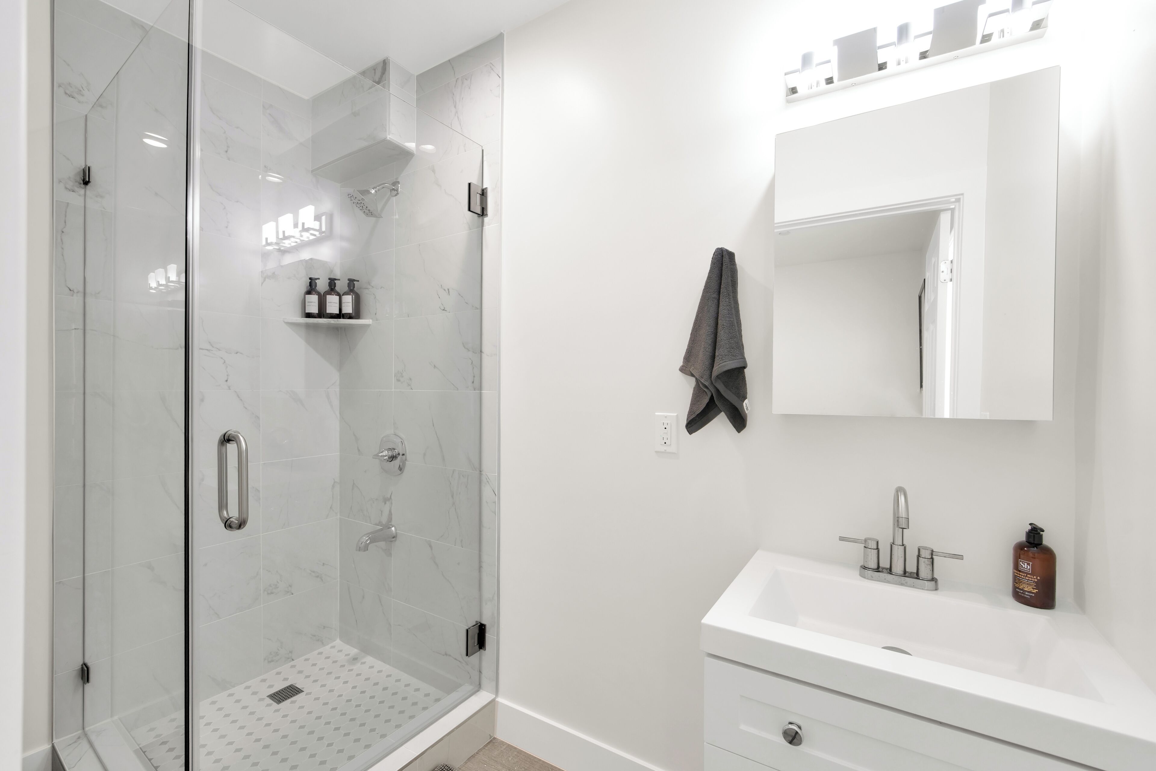 A modern bathroom with a glass-enclosed shower, a white sink with a mirror above it, and a towel hanging on the wall.