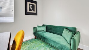 Une pièce avec un canapé vert, un fauteuil jaune, un tapis à motifs et un tableau encadré accroché au mur.