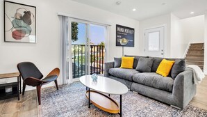 Un salon moderne avec un canapé gris, un fauteuil noir, une table basse blanche et un tapis à motifs.