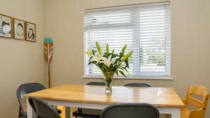A dining area with a wooden table, black and yellow chairs, a vase with flowers, and a window with blinds. - Charming 4 Bedroom Home Near Oxford (Oxford)