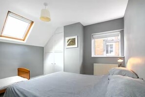 Een slaapkamer met een bed, een bureau, een stoel, een raam en een radiator.