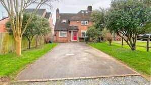 A two-story brick house with a red door, a paved driveway, and a fenced yard. - Charming 4 Bedroom Home Near Oxford (Oxford)