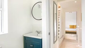 A modern bathroom with a white sink, teal cabinet, and a round mirror on the wall. - Charming 4 Bedroom Home Near Oxford (Oxford)