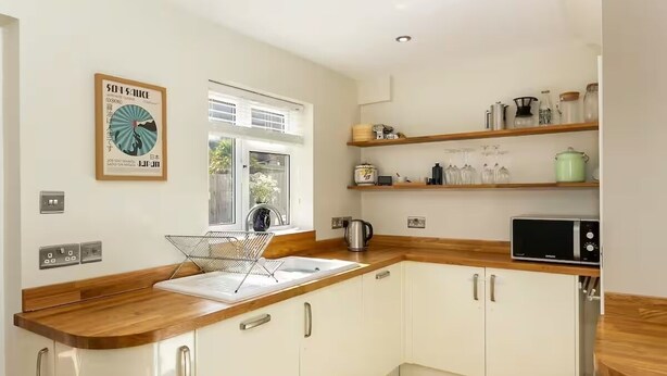 A modern kitchen with white cabinets, wooden countertops, and a window providing natural light. - Charming 4 Bedroom Home Near Oxford (Oxford)