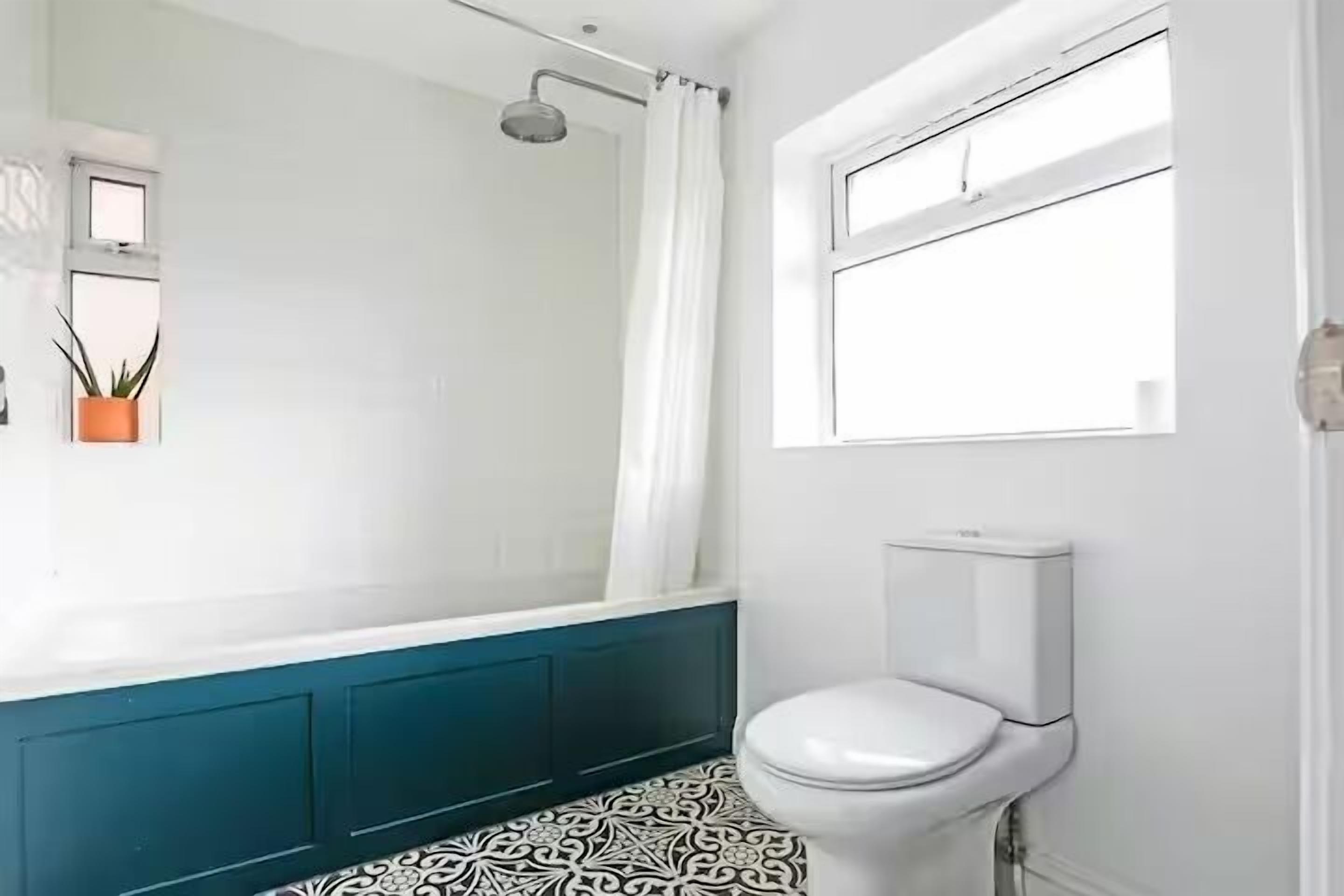 A bathroom with a white toilet, a shower with a curtain, a window, and a potted plant.
