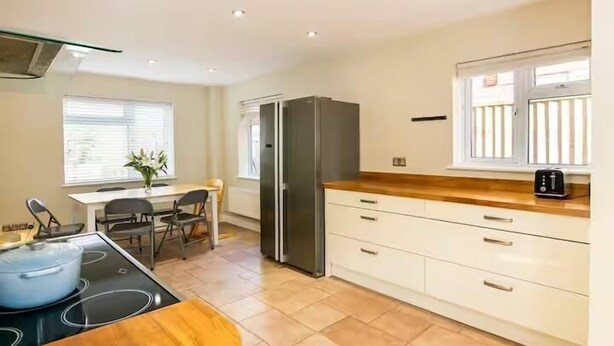 A modern kitchen with a built-in stove, a refrigerator, and a dining area with a table and chairs. - Charming 4 Bedroom Home Near Oxford (Oxford)