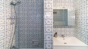 A bathroom with patterned tiles, a bathtub, a shower, and a sink with a mirror.
