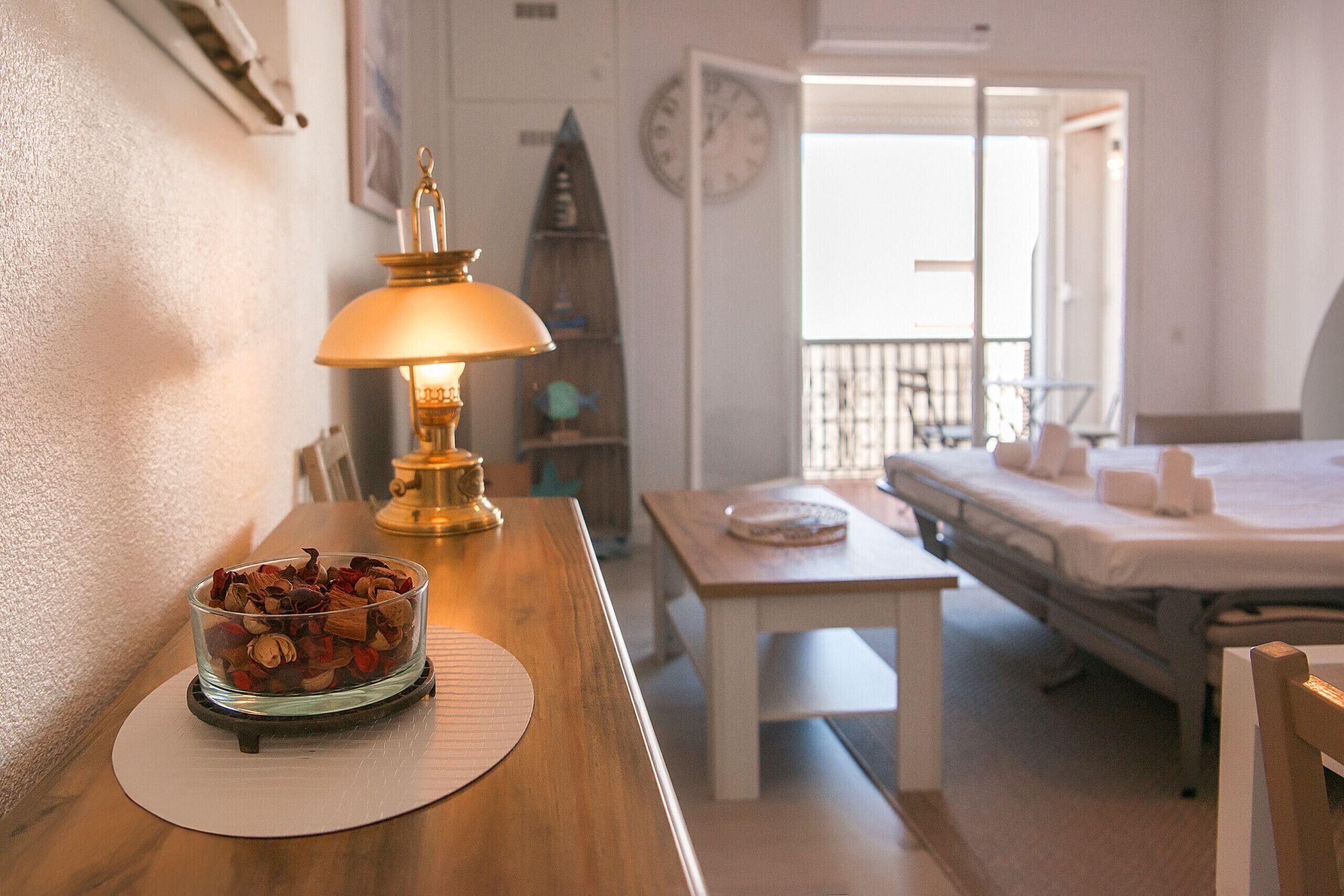 Een hotelkamer met een houten tafel, een lamp, een schaal met snacks, een bed en uitzicht op buiten.